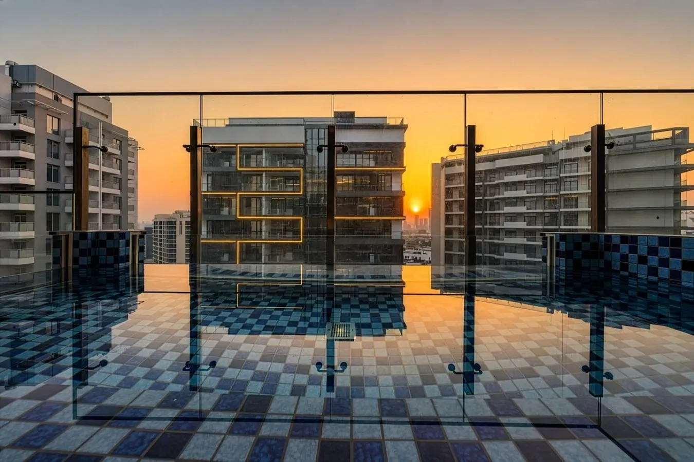 Una terraza en la azotea con barandillas de vidrio da a edificios de apartamentos al atardecer.