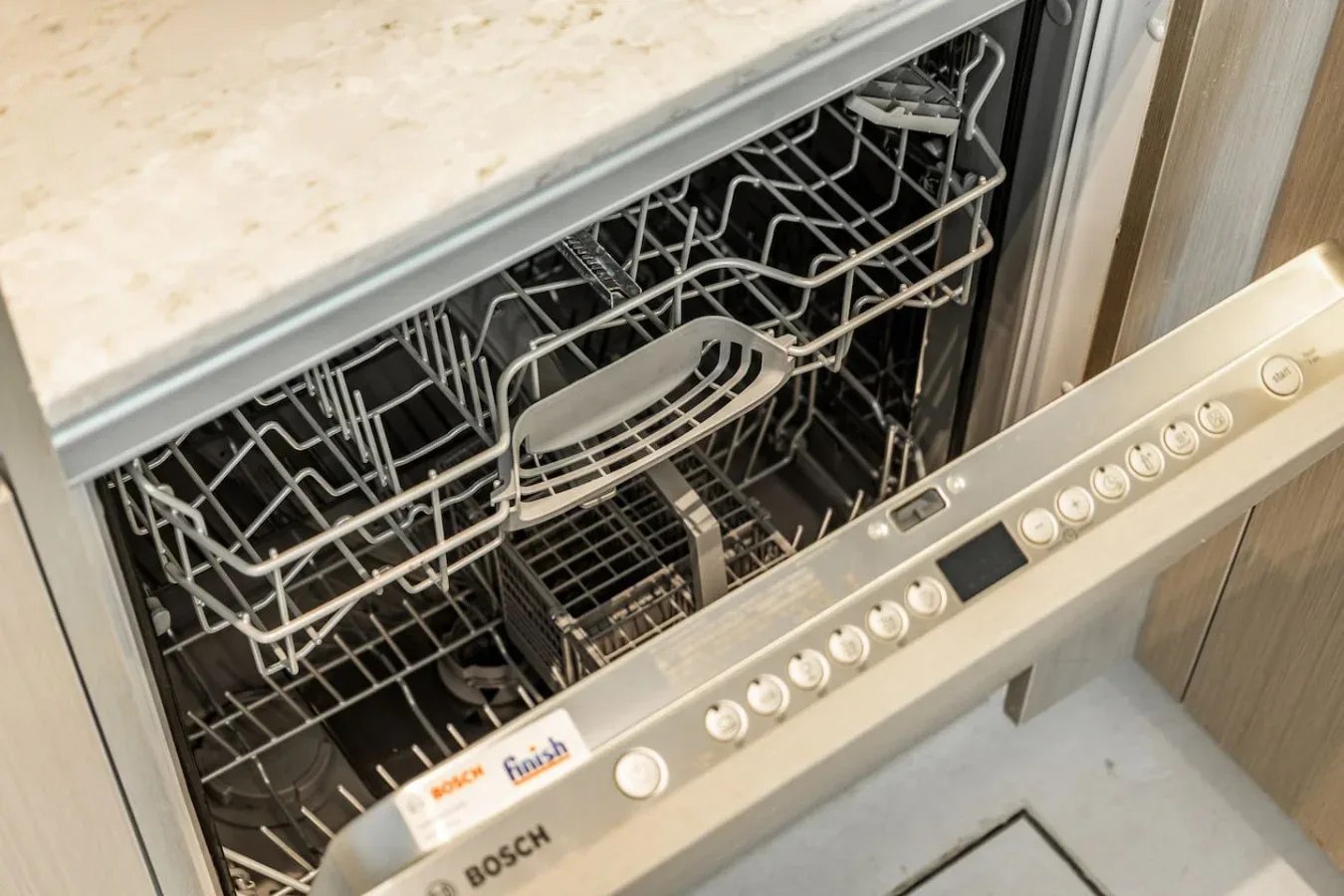 Un lavavajillas abierto con las bandejas extendidas bajo una encimera de cocina.