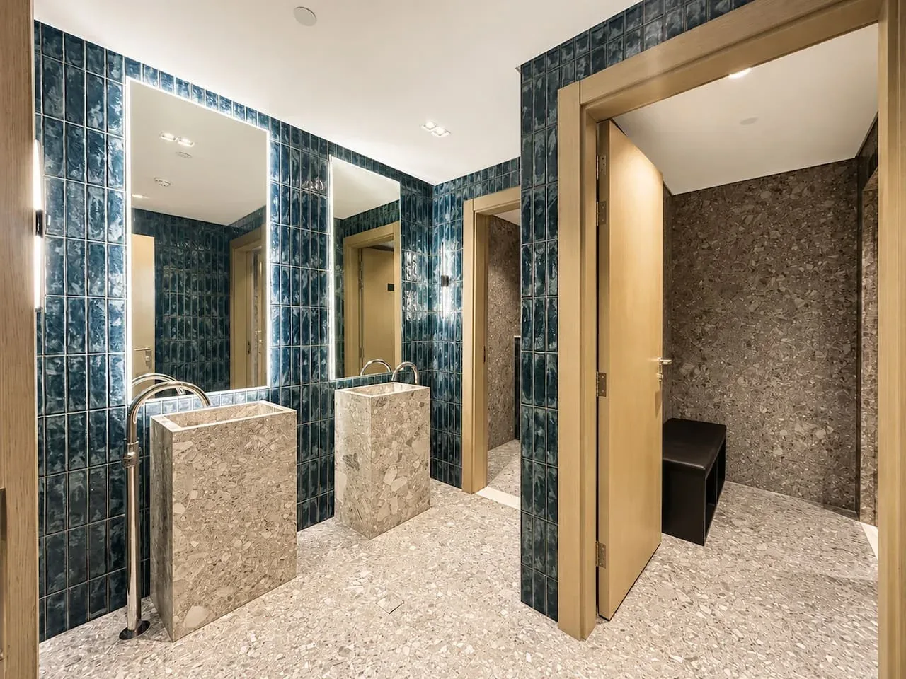 Zona de tocadores de baño alicatada con lavabos de piedra y una puerta a una habitación contigua.