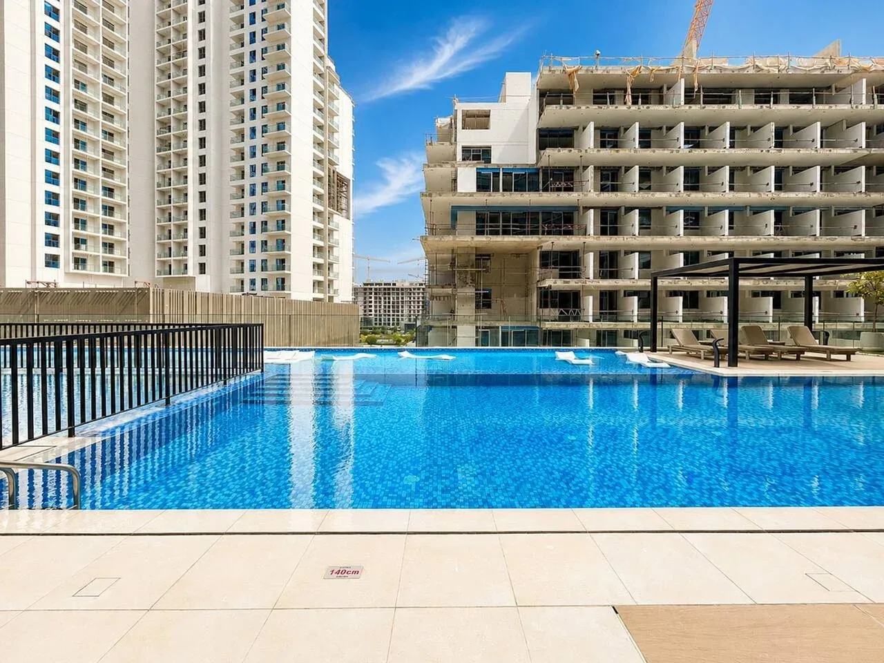 Una piscina al aire libre está junto a edificios altos, uno de ellos en construcción.