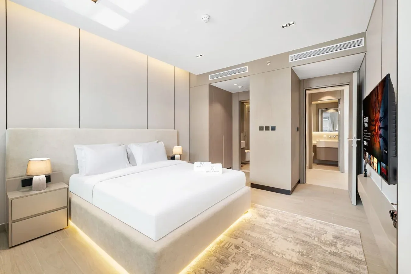 Un dormitorio luminoso con una cama grande, mesillas de noche y un televisor en la pared.