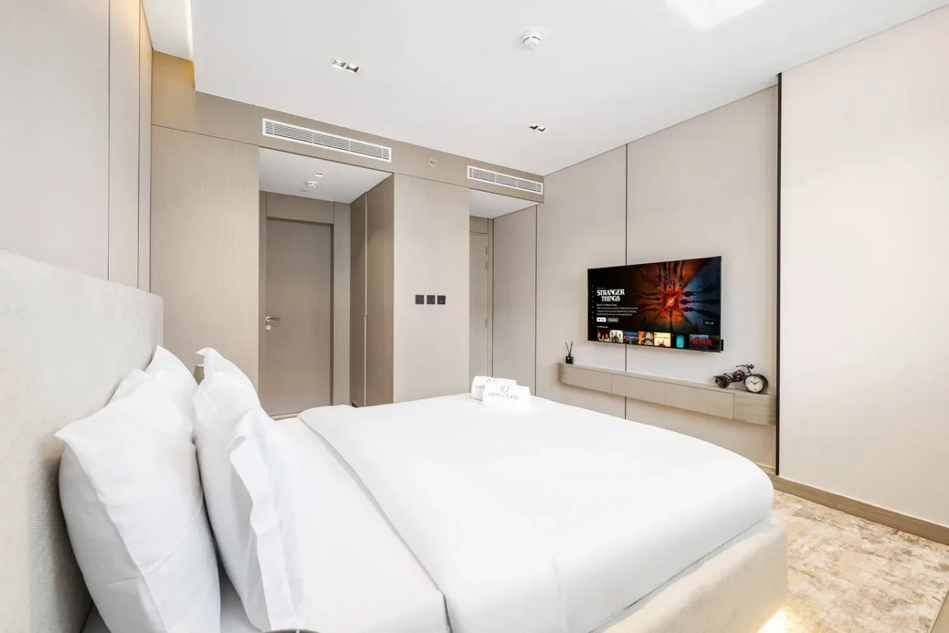 Un dormitorio luminoso con una cama grande y un televisor montado en la pared.