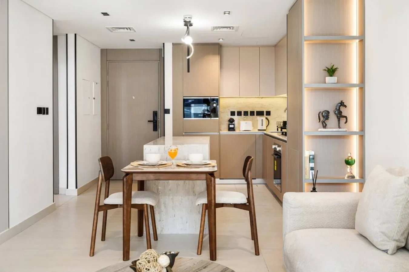 Un comedor con mesa de madera y asientos se abre a una cocina compacta.