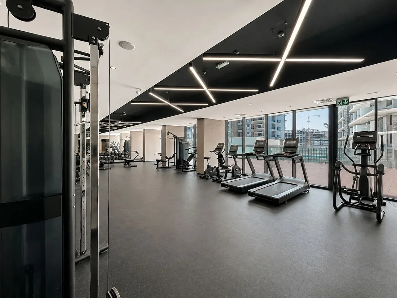 Un gimnasio moderno con cintas de correr y máquinas de ejercicio junto a grandes ventanales.