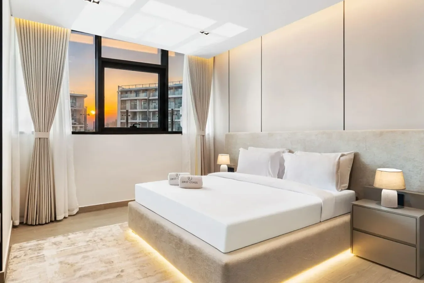 Dormitorio con una cama grande, mesitas de noche y una ventana con edificios a la vista.