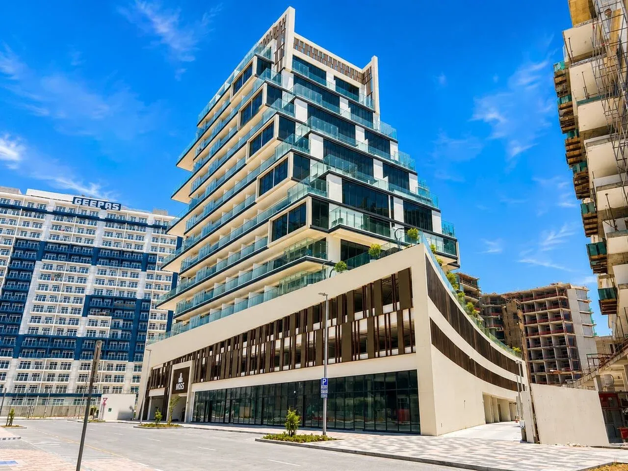 Un edificio moderno de varias plantas con balcones de vidrio junto a una calle pavimentada.