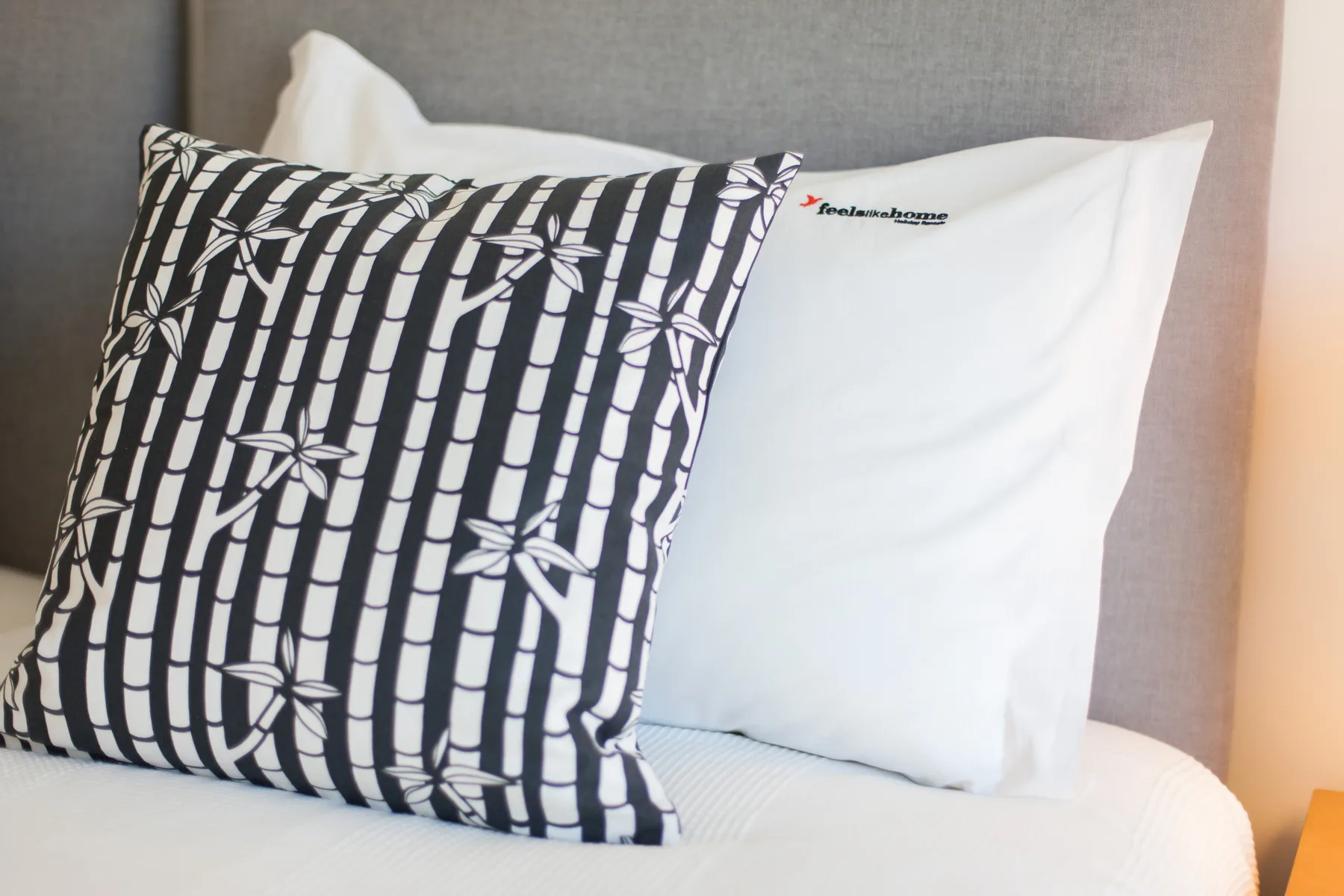 Close-up of a bed with white pillows and a patterned black-and-white cushion.