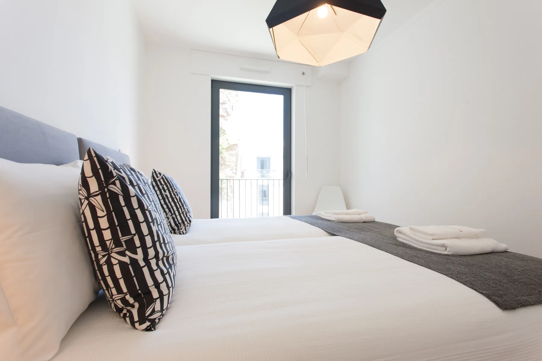 A bright bedroom with a bed, patterned pillows, and a window.