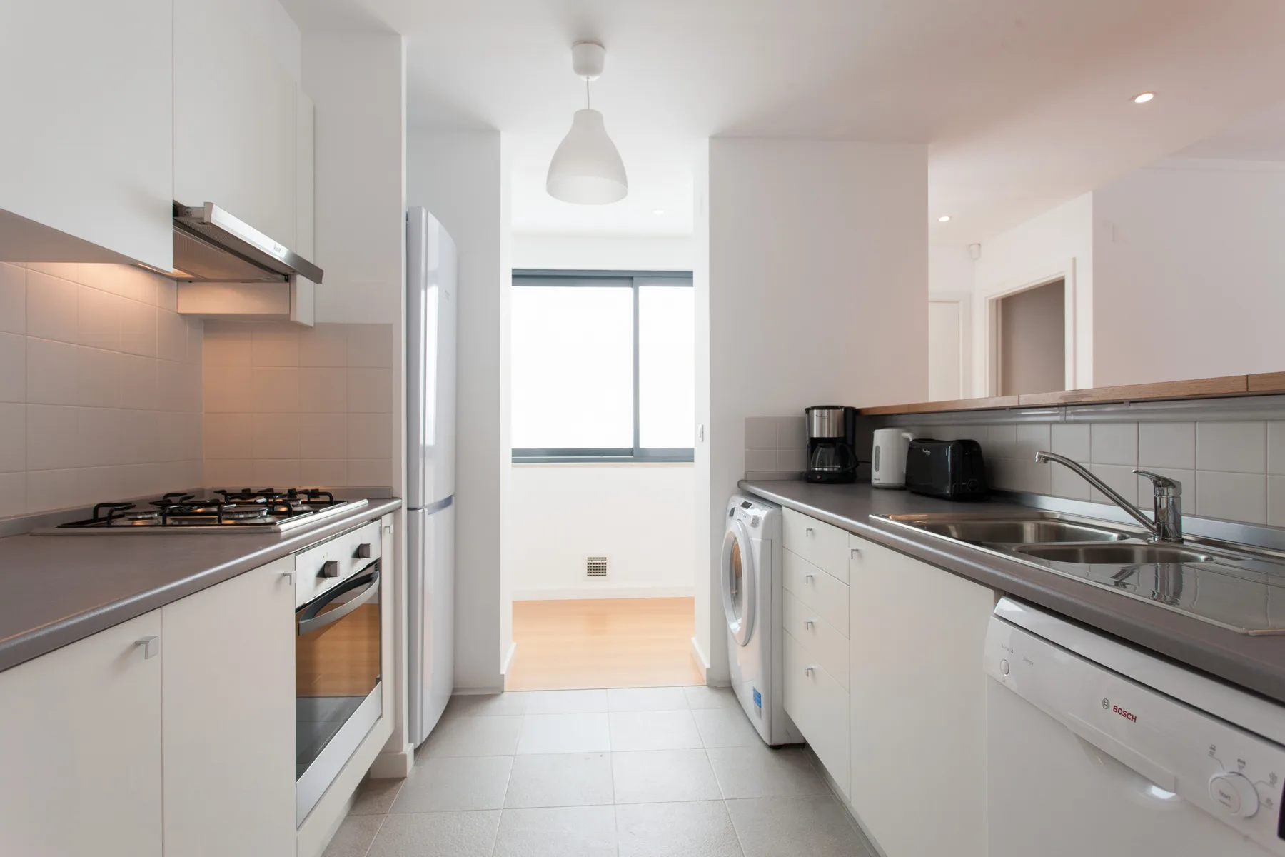 A bright galley kitchen with white cabinets and a window at the far end.