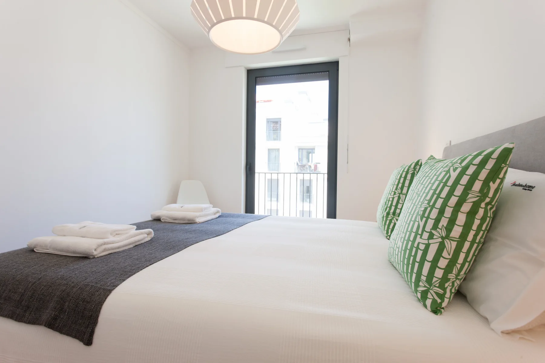 A bedroom with a neatly made bed and green patterned pillows.