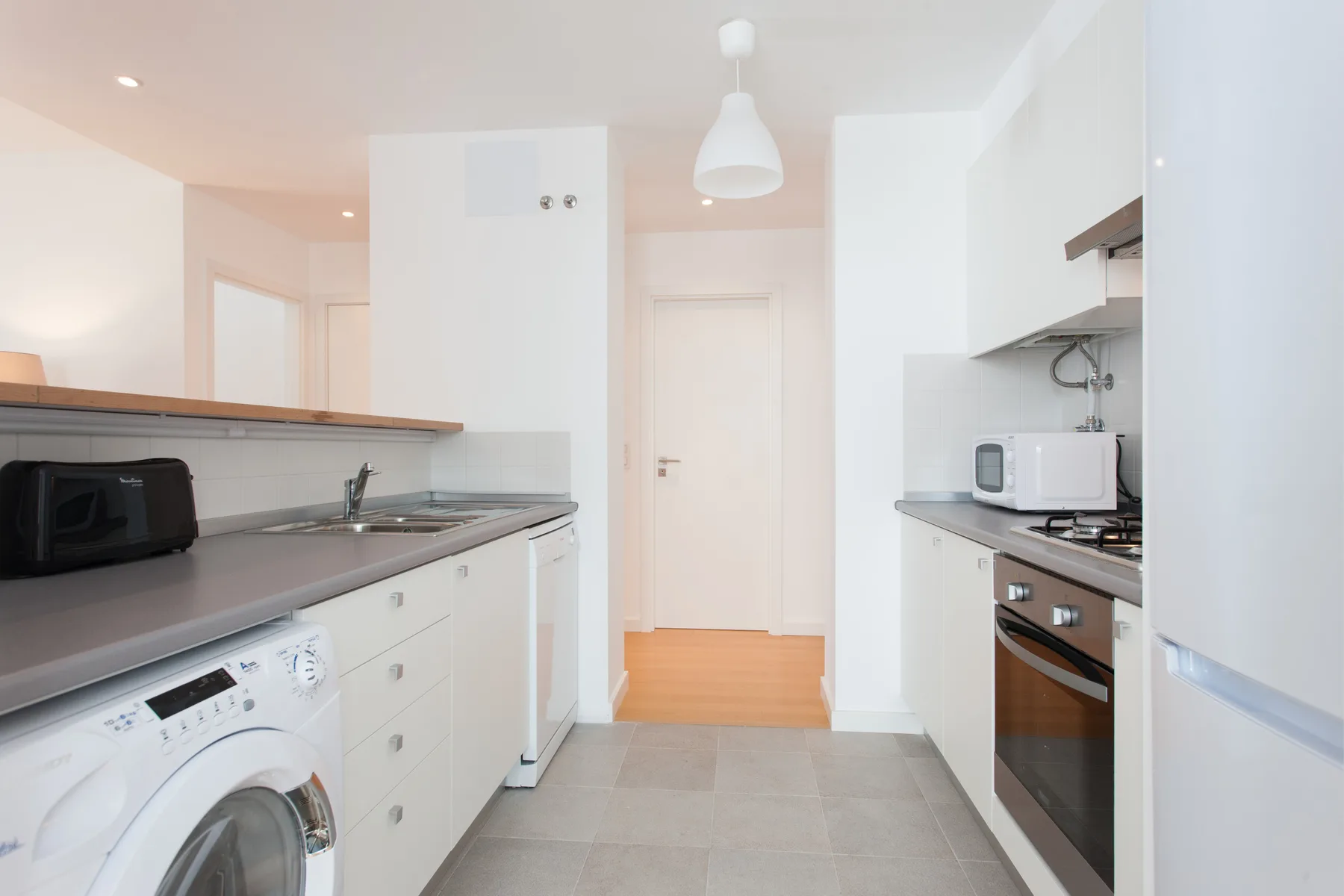A bright kitchen with countertops, appliances, and a door at the far end.