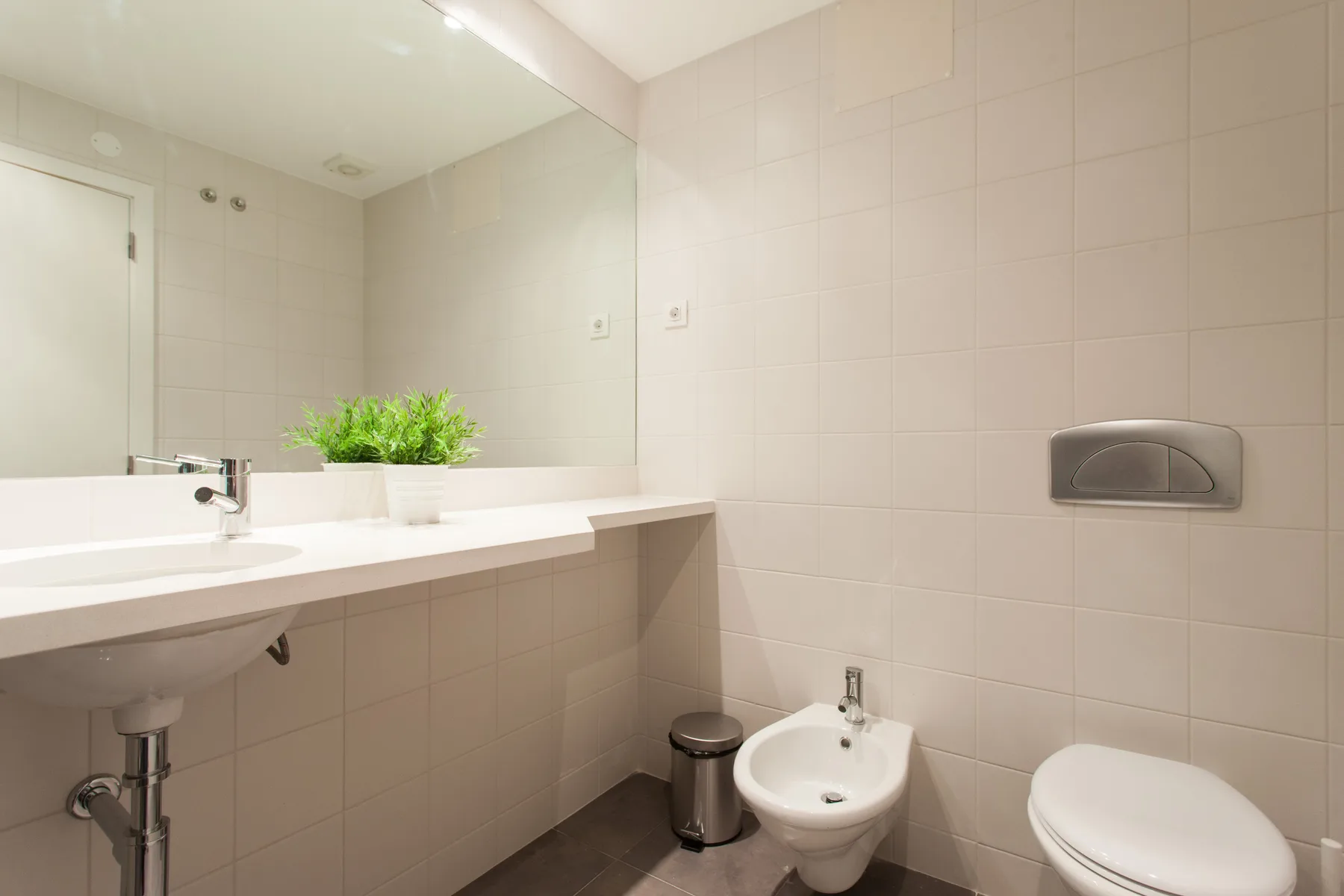 A tiled bathroom with a long sink counter and toilet.
