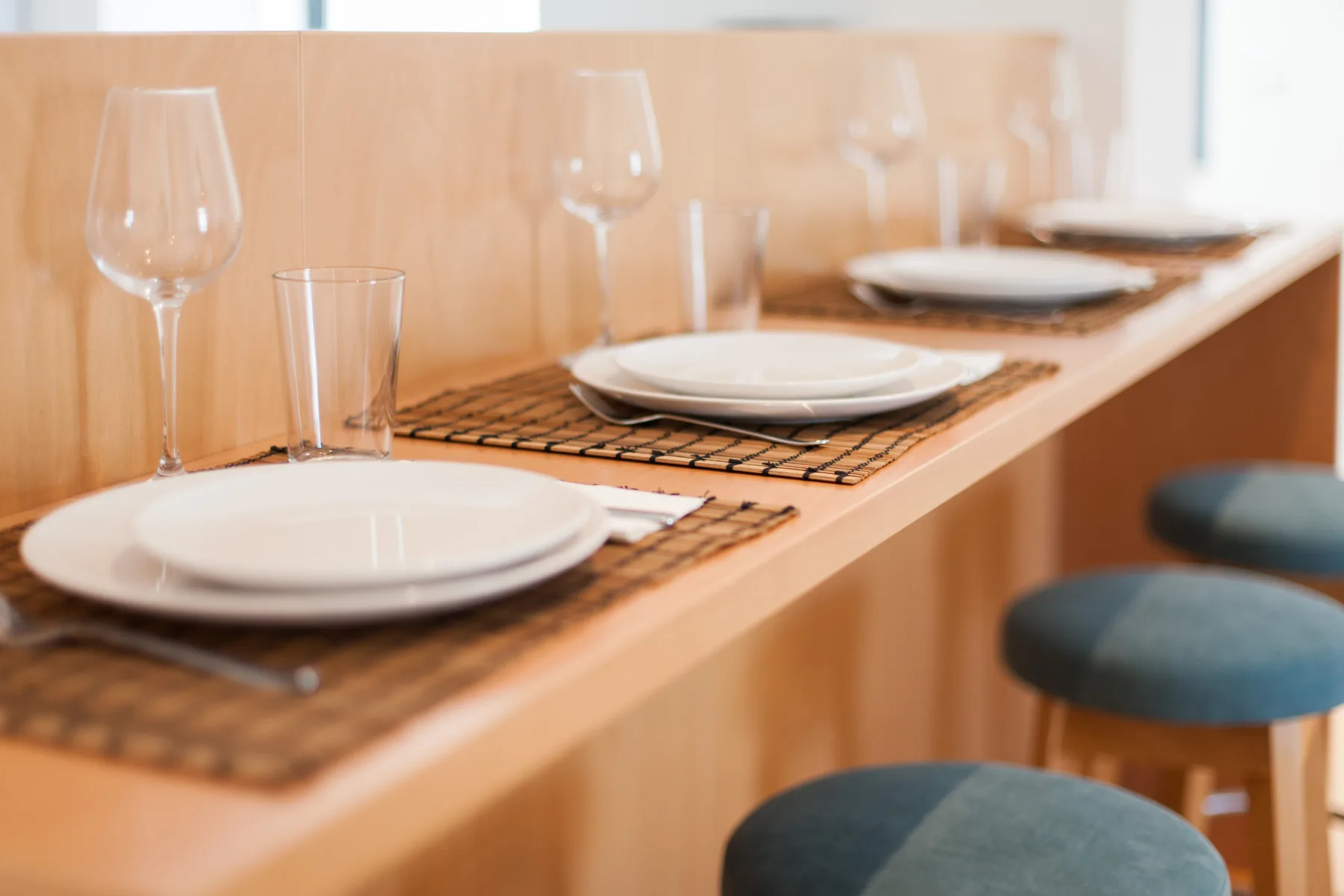 A dining counter is set with plates, glasses, and woven placemats.