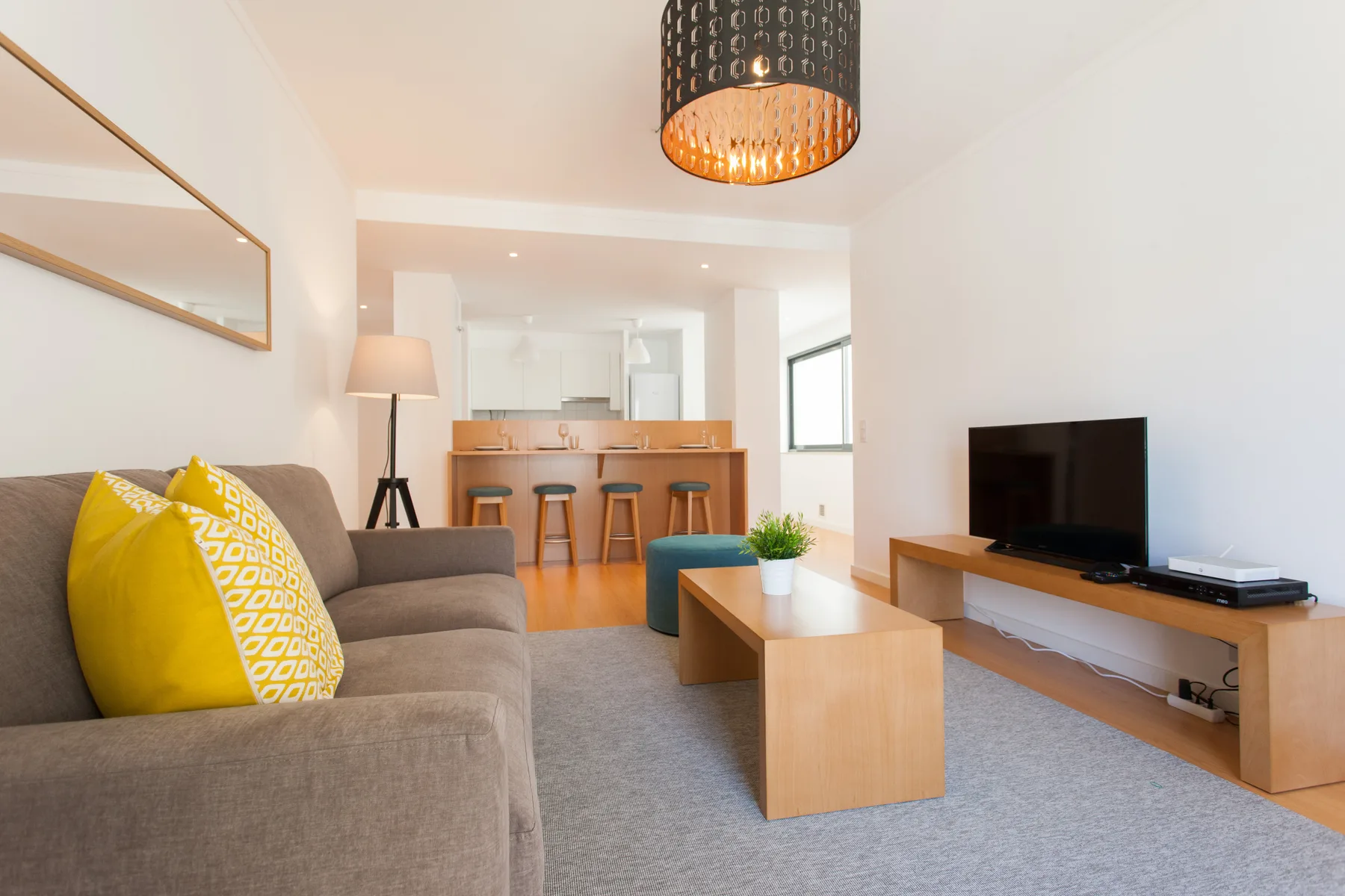A living room with seating, a coffee table, and a television facing an open kitchen.
