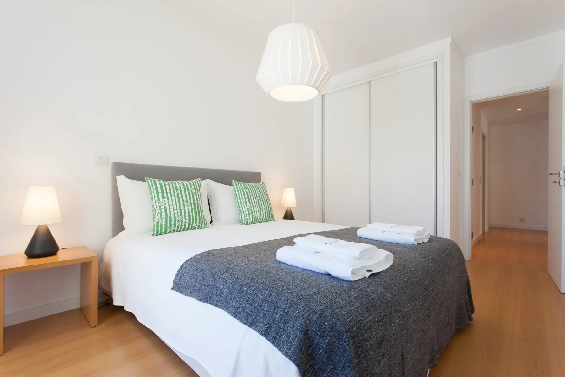 A bright bedroom with a neatly made bed and green accent pillows.