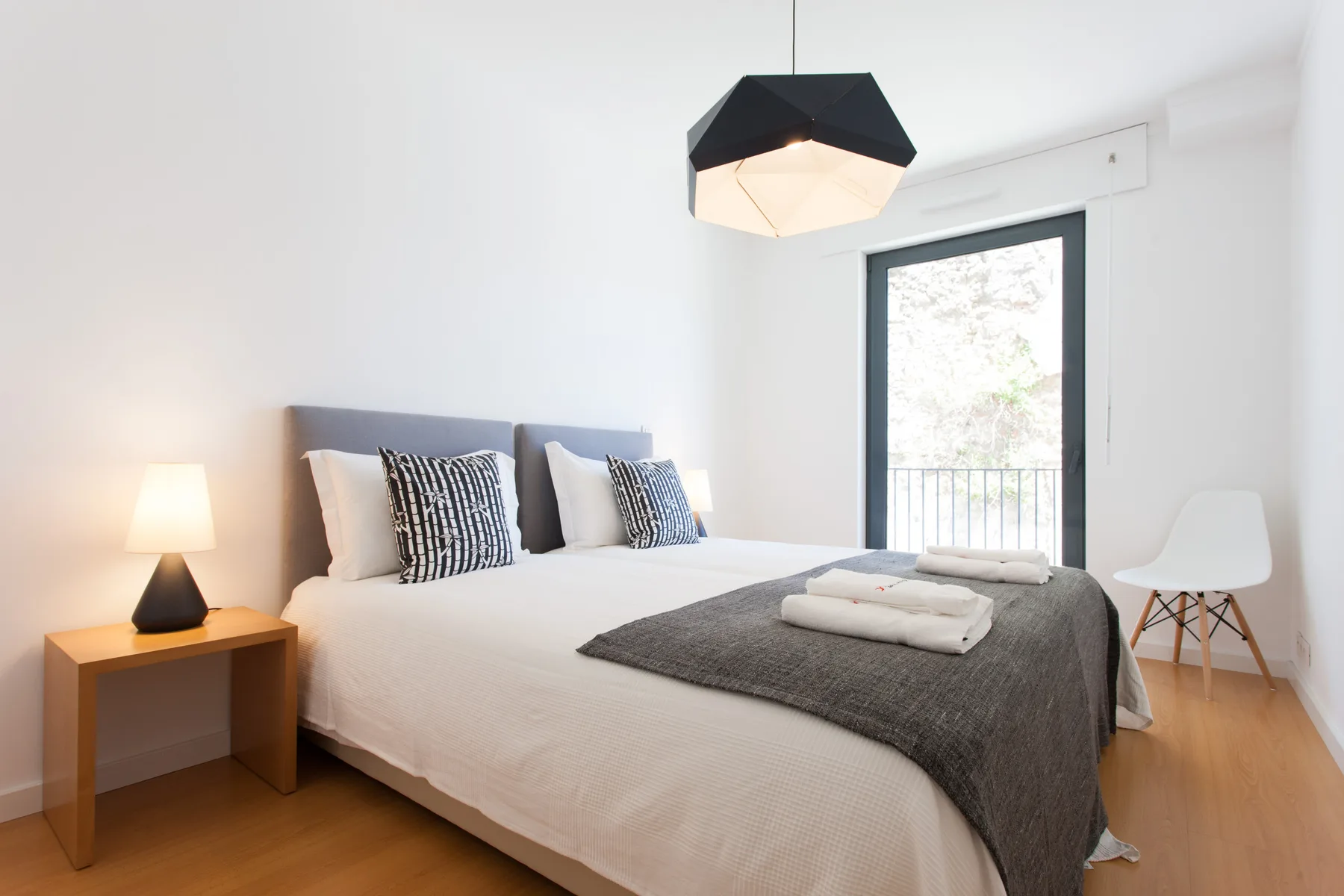 A bright bedroom with a double bed, bedside table, and balcony doors.