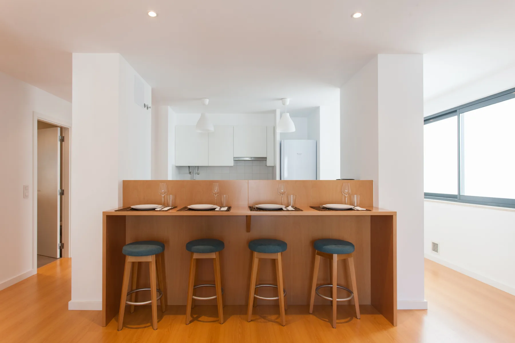 A bright kitchen with a wooden breakfast bar and four stools.
