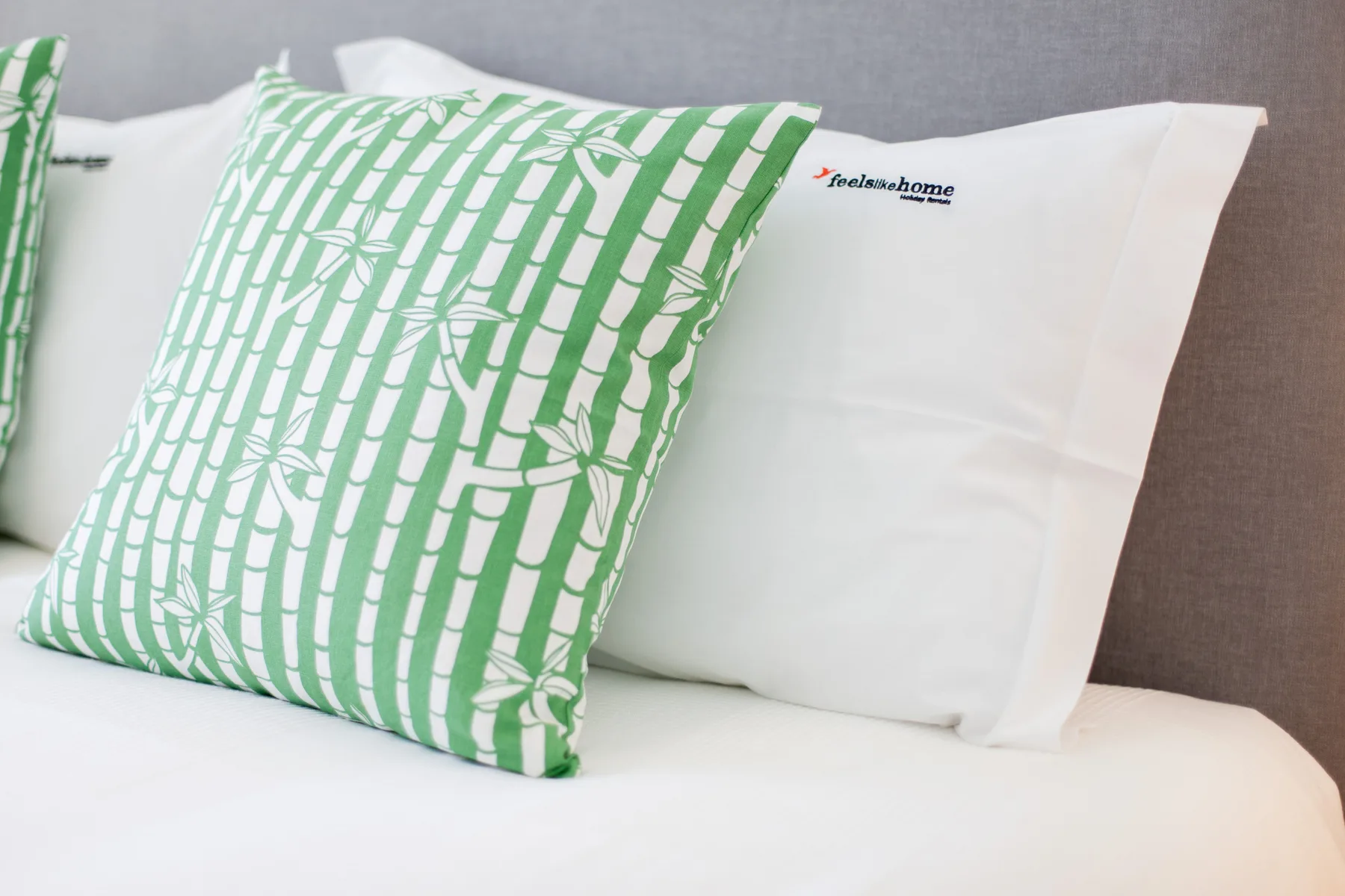 A bed with white pillows and a green patterned decorative cushion.