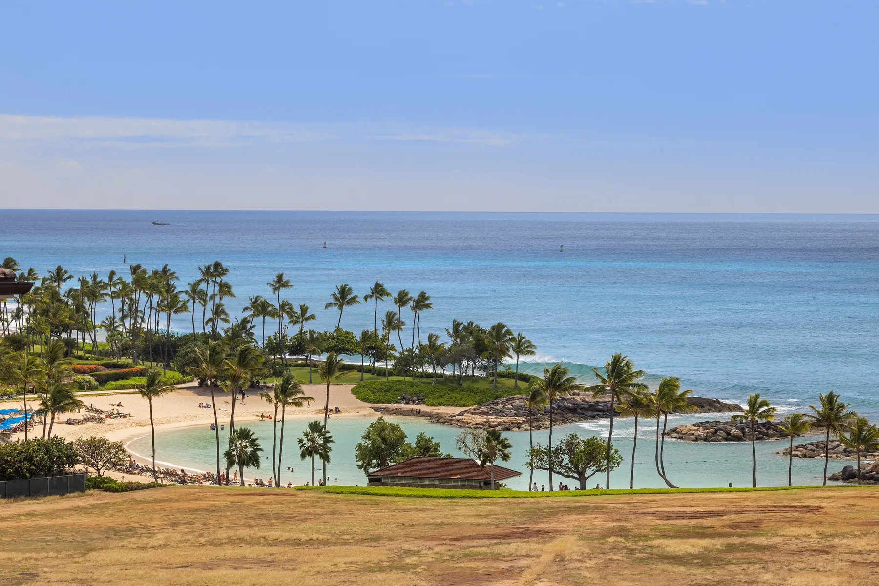 Un paisaje tropical junto al mar, con palmeras, una laguna y el océano al fondo.