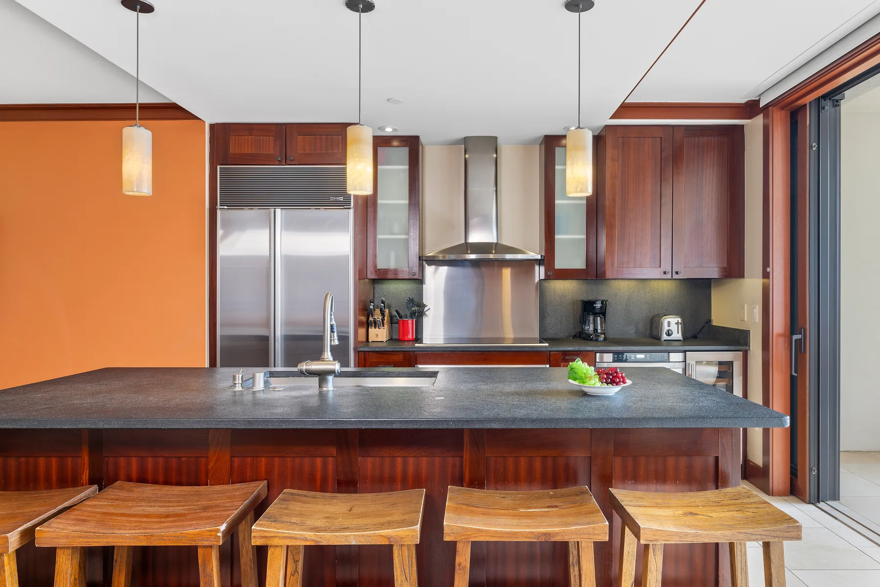 Una cocina moderna con una isla amplia, taburetes de madera y lámparas colgantes.