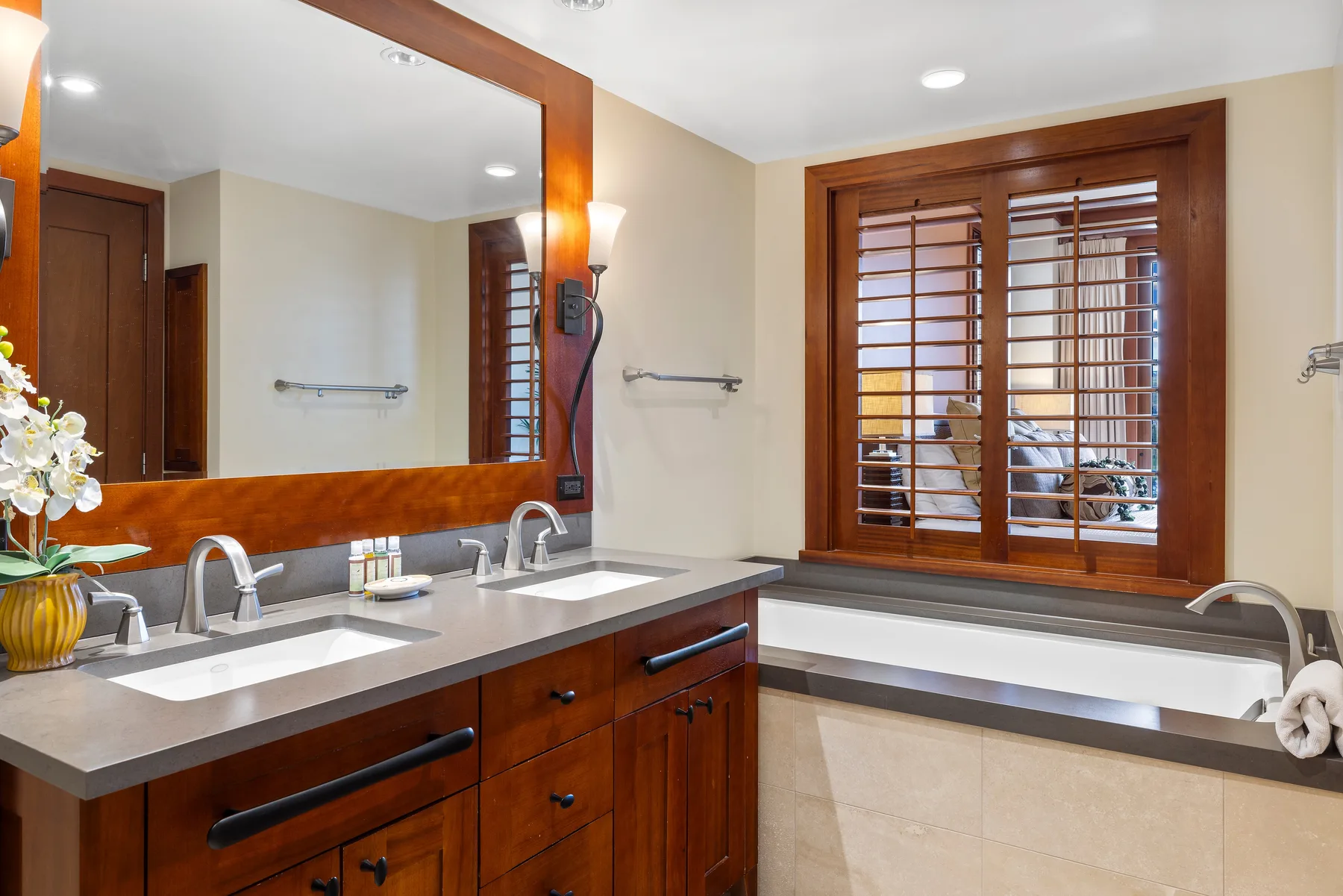 Un tocador de baño y una bañera están bajo una gran ventana enmarcada en madera.