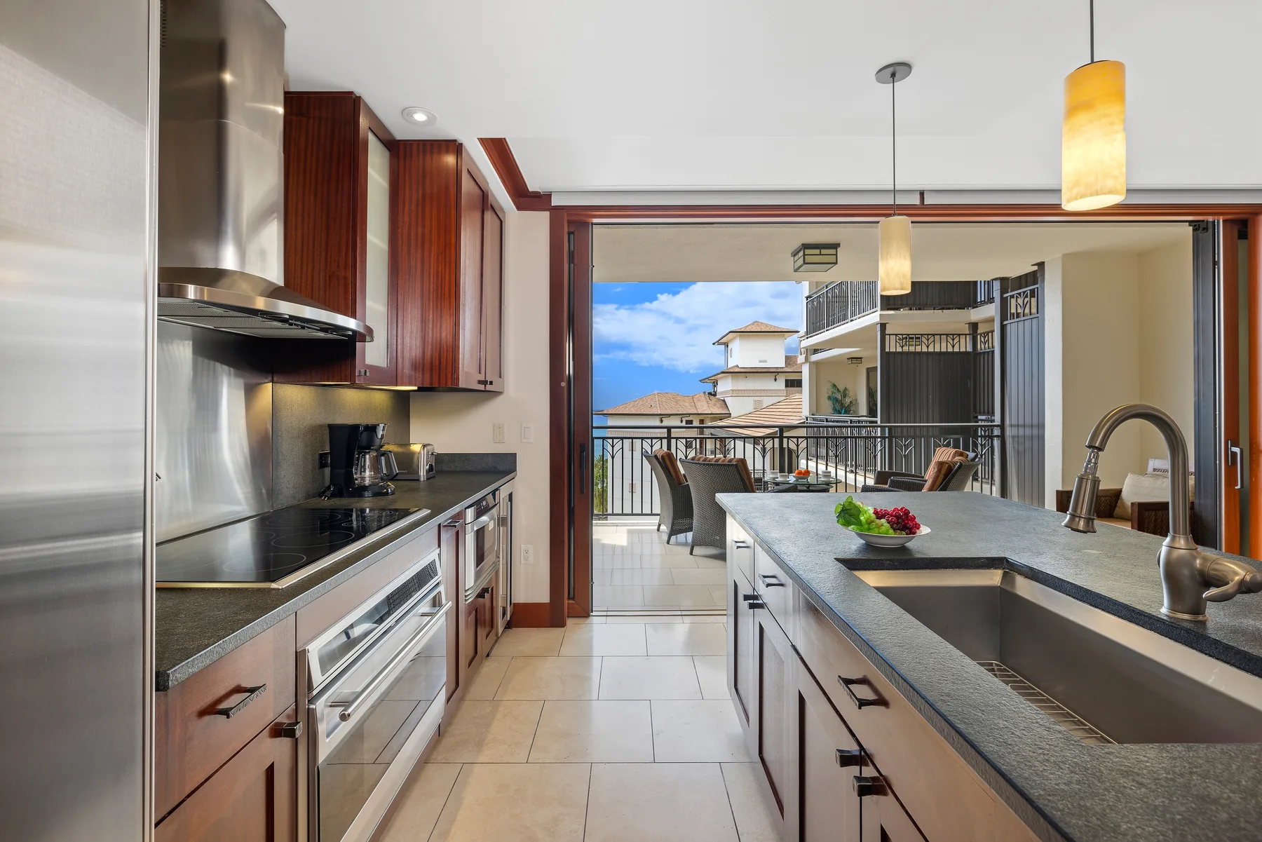 Una cocina moderna se abre a un balcón, con una isla larga y un fregadero en primer plano.