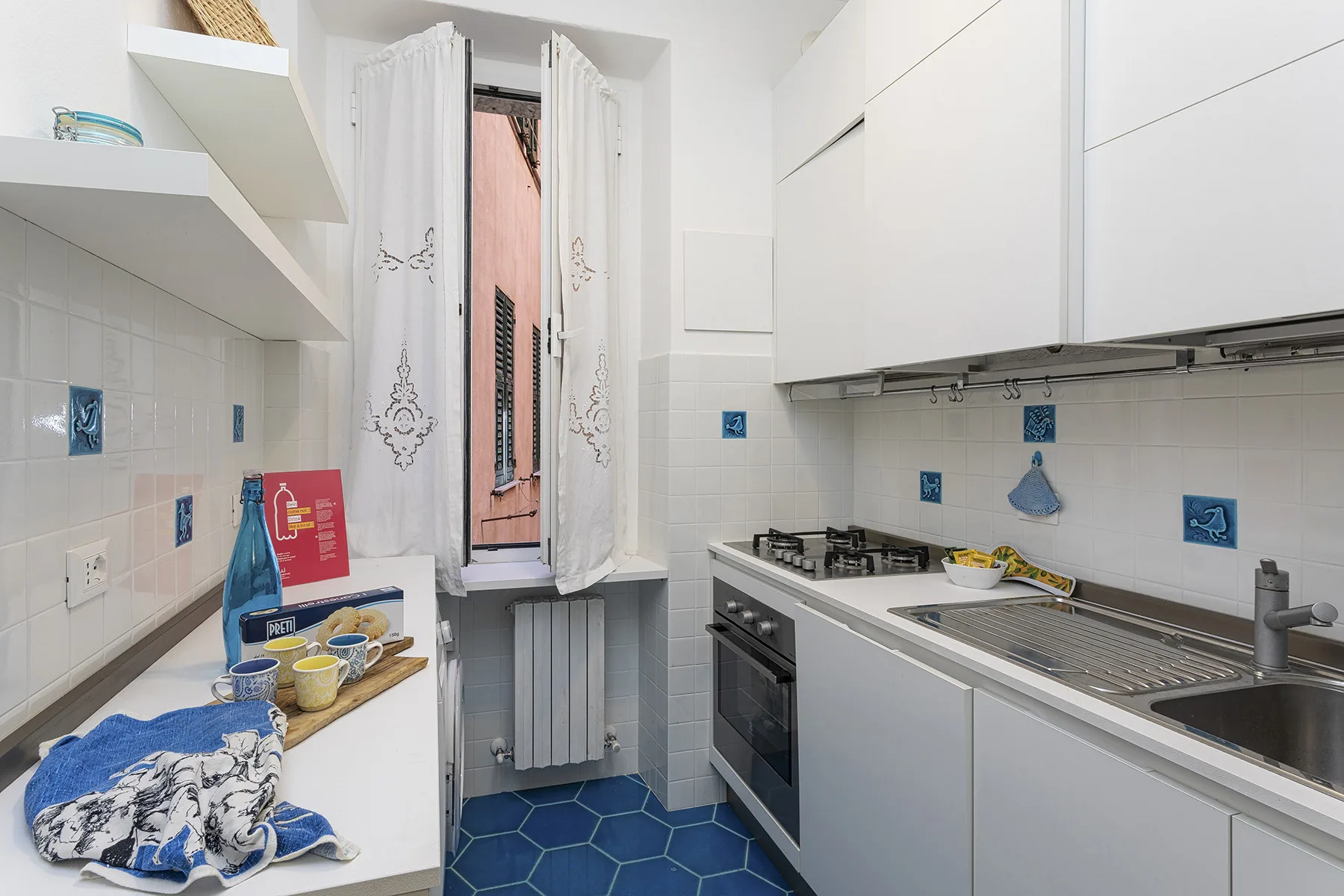 A bright kitchen with white cabinets, a countertop, and a window with curtains.