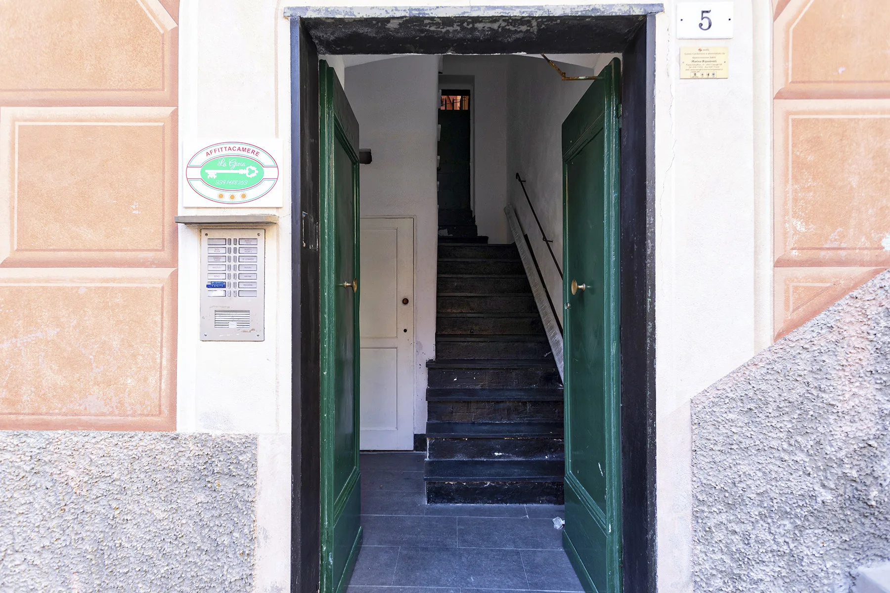 An open entrance leads to a dim stairwell with dark steps and green doors.