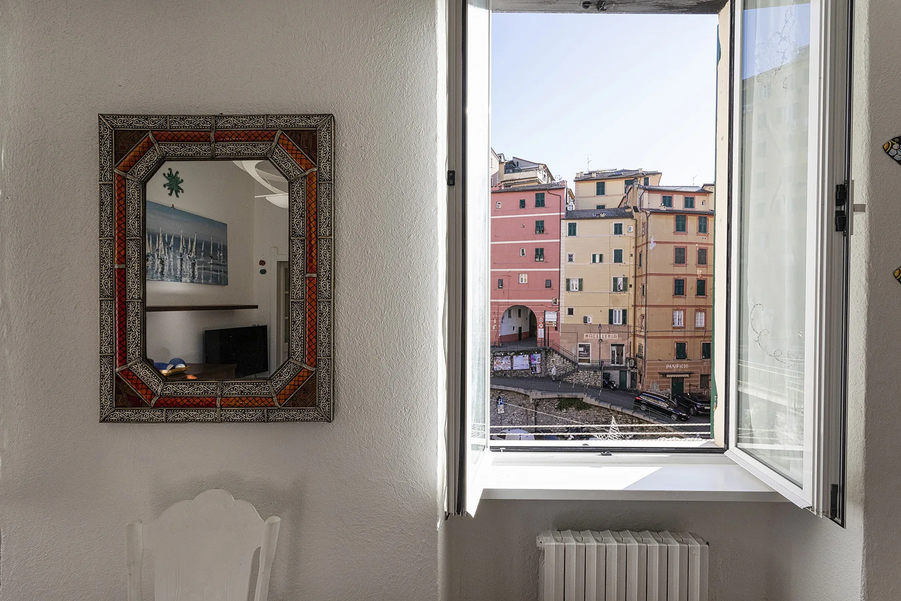 A bright room with an open window overlooking colorful buildings.