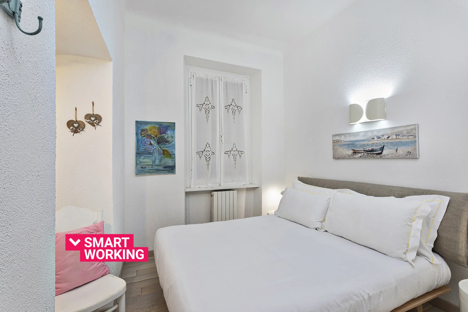 A bright bedroom with a neatly made bed and framed artwork on the walls.