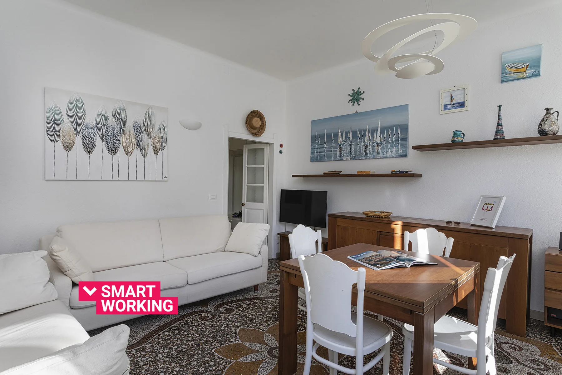 A living and dining room with a wooden table, white seating, and framed wall art.