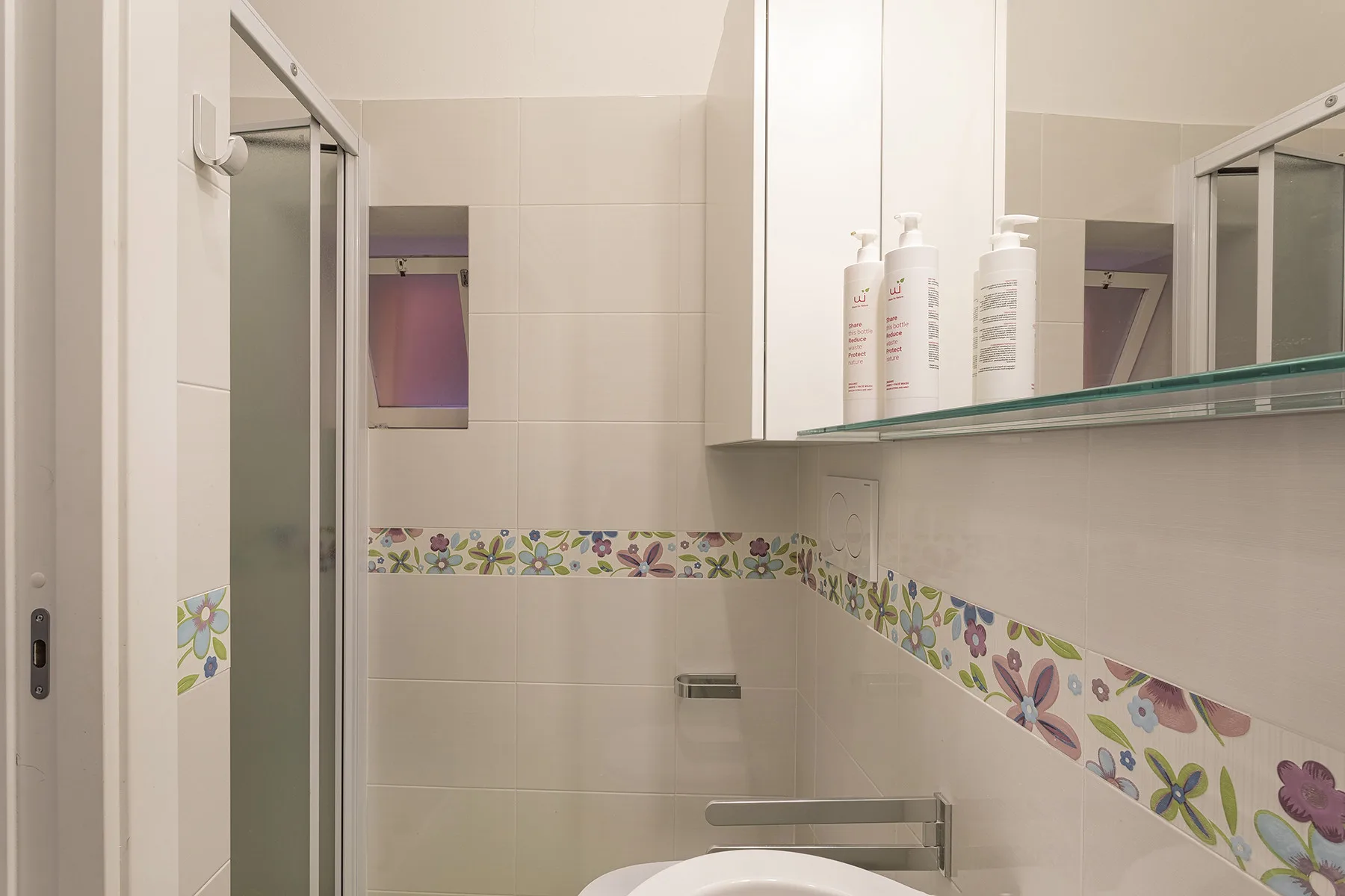 A tiled bathroom with a glass shower and a floral decorative border.