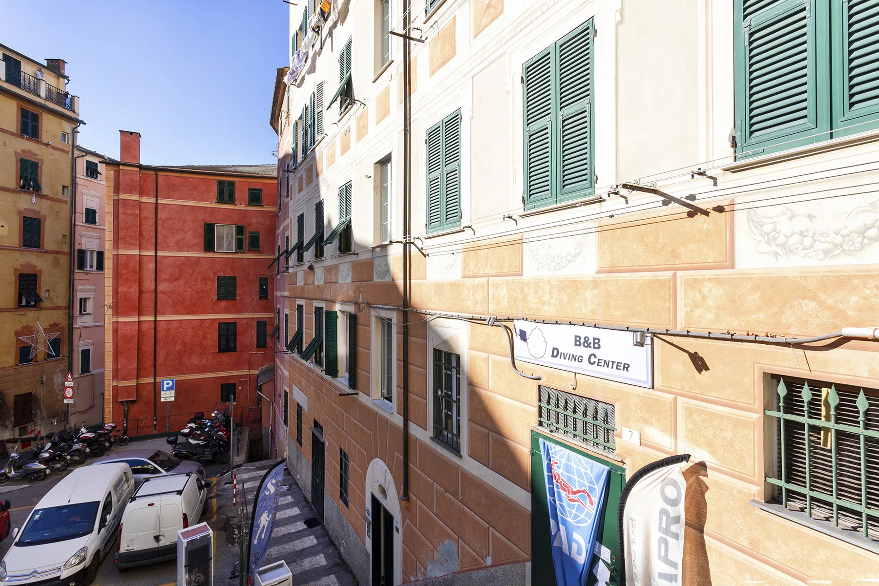 A sunlit city street lined with multistory buildings and parked vehicles.