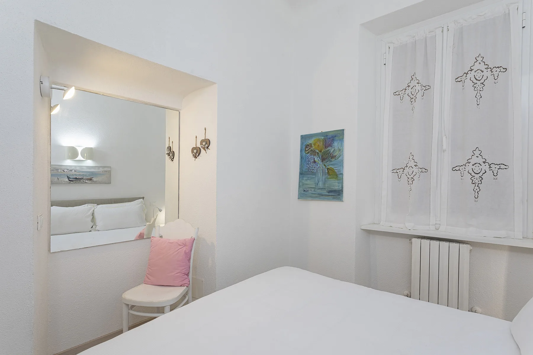 A bright bedroom with a bed, a window, and a small chair.