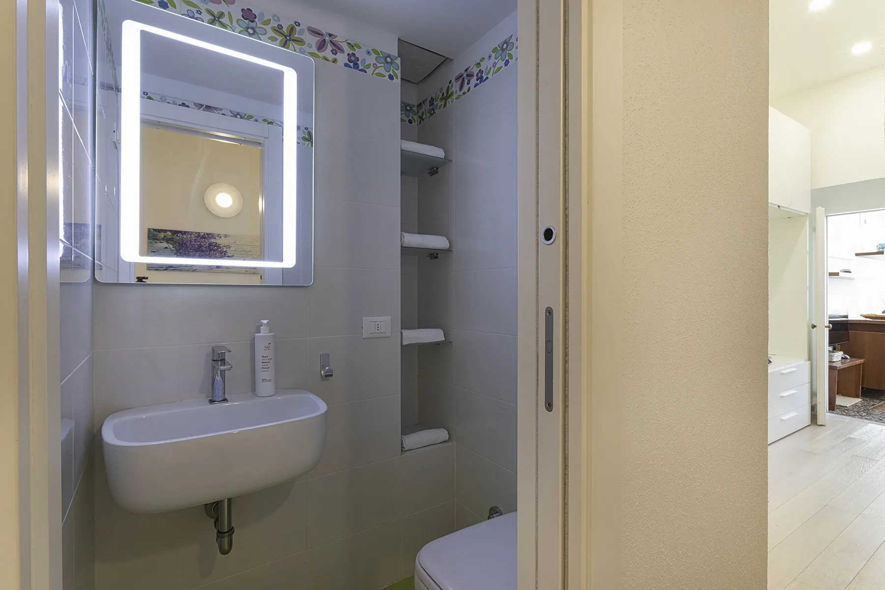 A bathroom with a wall-mounted sink and an illuminated mirror.