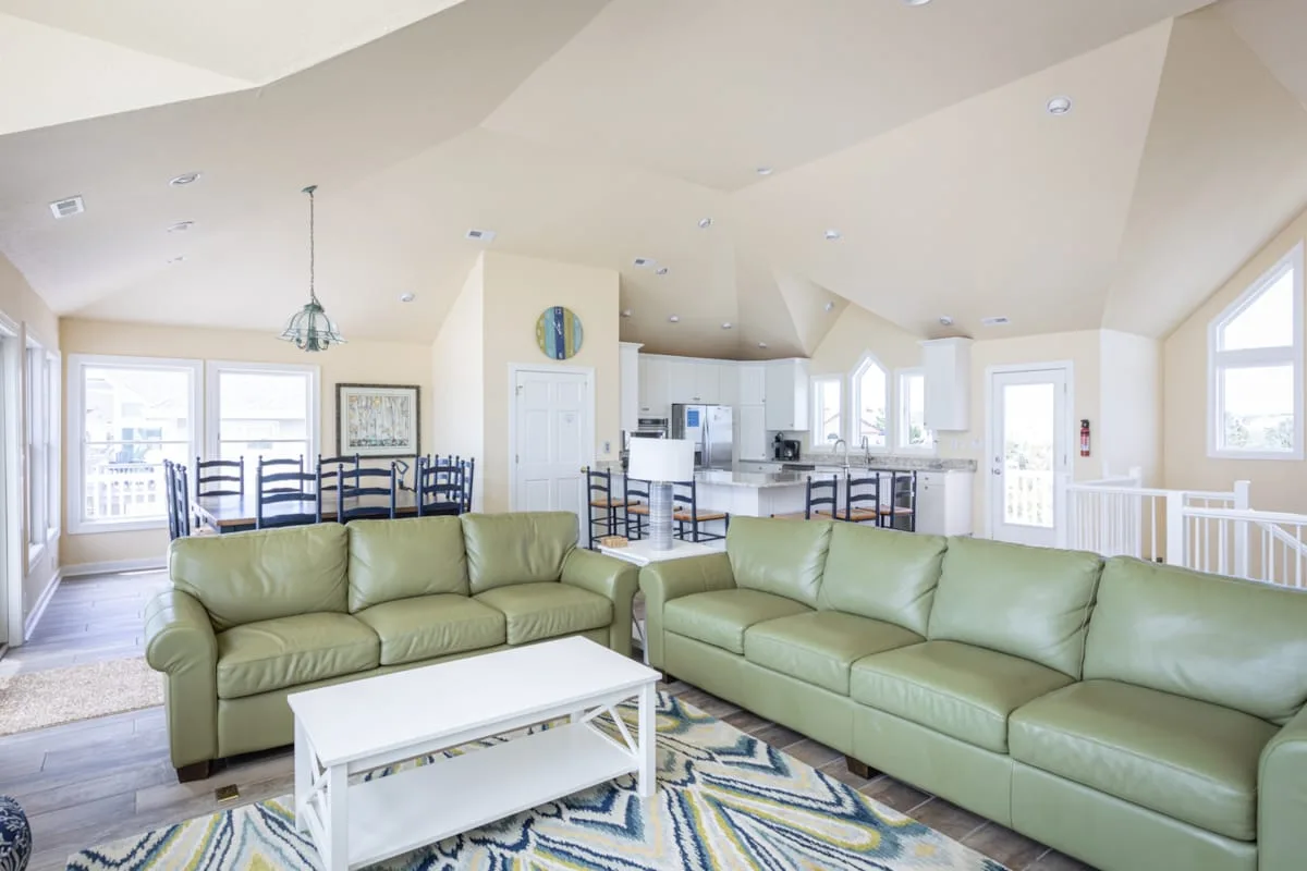 Una sala luminosa con asientos verdes y una cocina abierta al fondo.