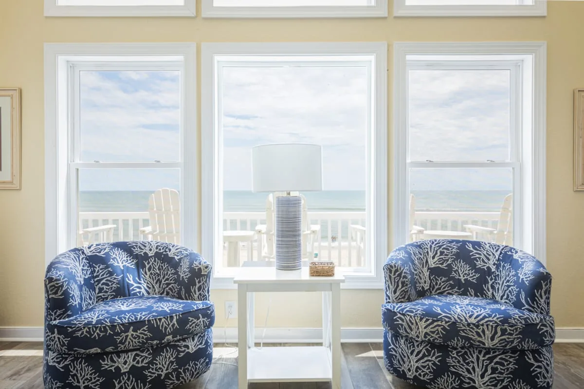 Una zona de estar con asientos estampados y una mesa pequeña frente a grandes ventanas con vista al agua.
