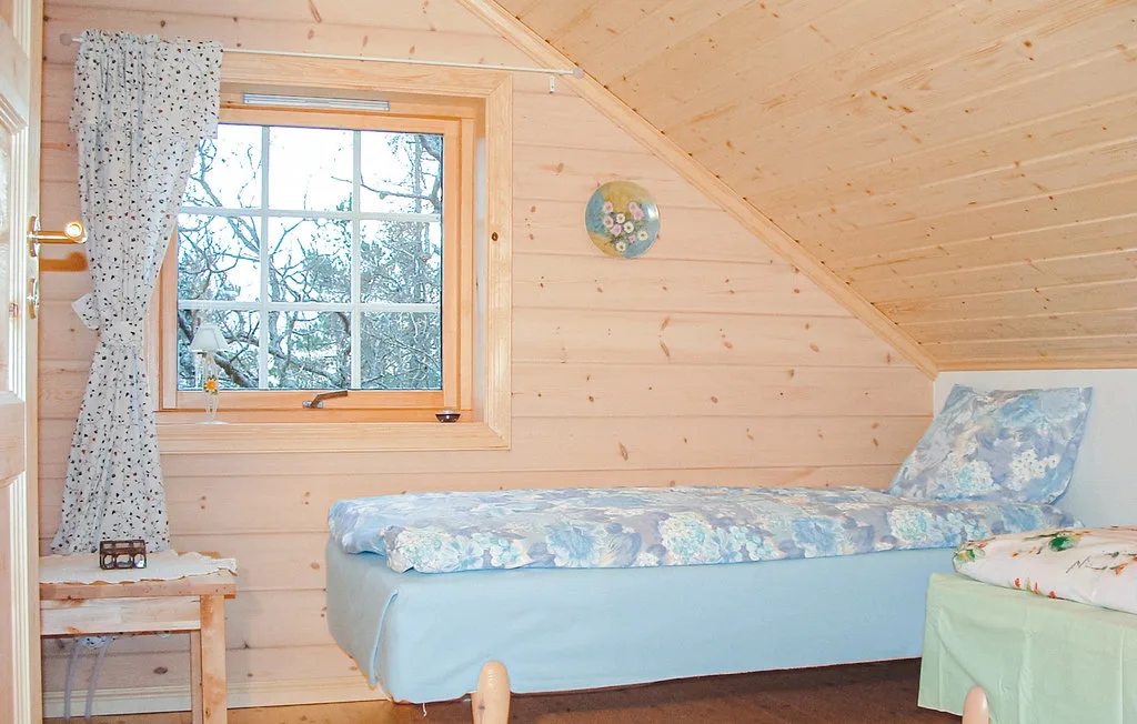A bedroom with a bed beneath a sloped wooden ceiling and a window.