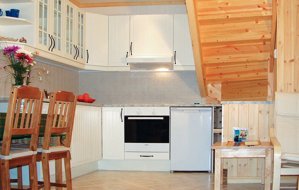 A kitchen with white cabinets, a cooking range, refrigerator, and wooden seating.
