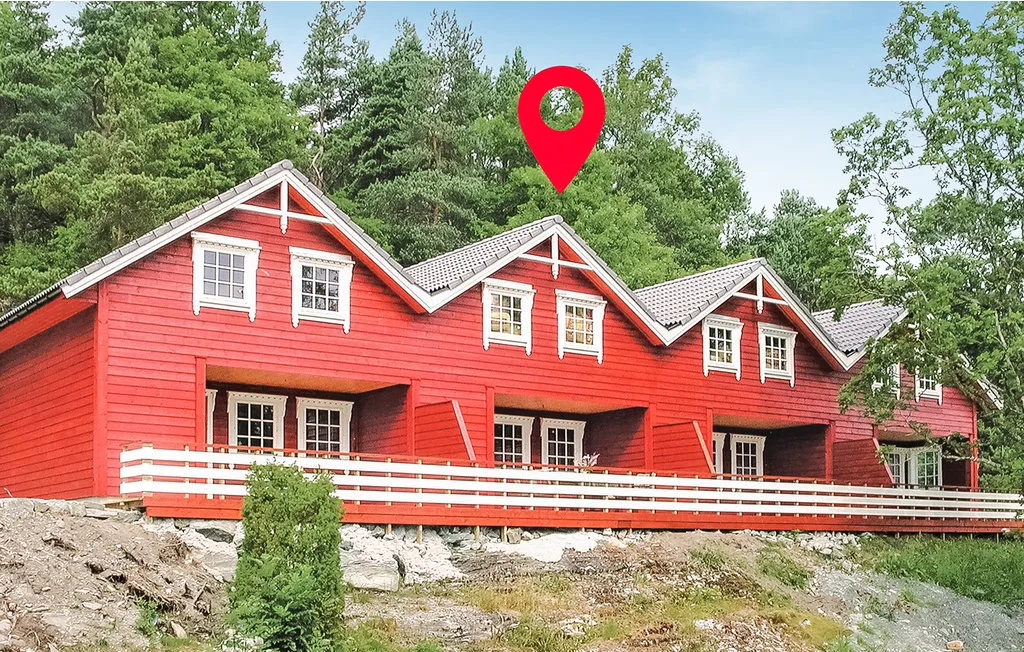 A red multi-section building stands among trees beside a rocky slope.