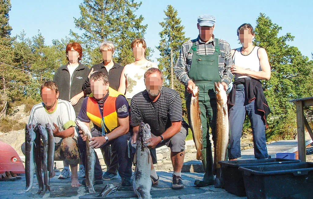 A group poses outdoors with freshly caught fish beside fishing equipment.
