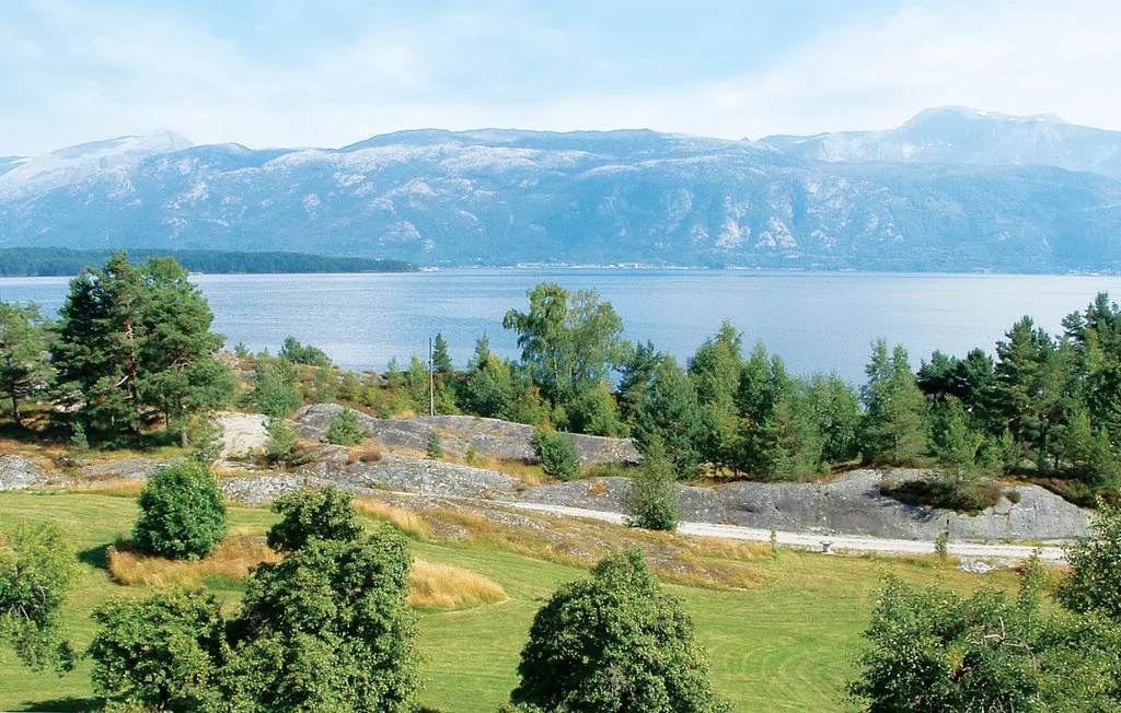 A green lakeside landscape with trees and mountains across the water.
