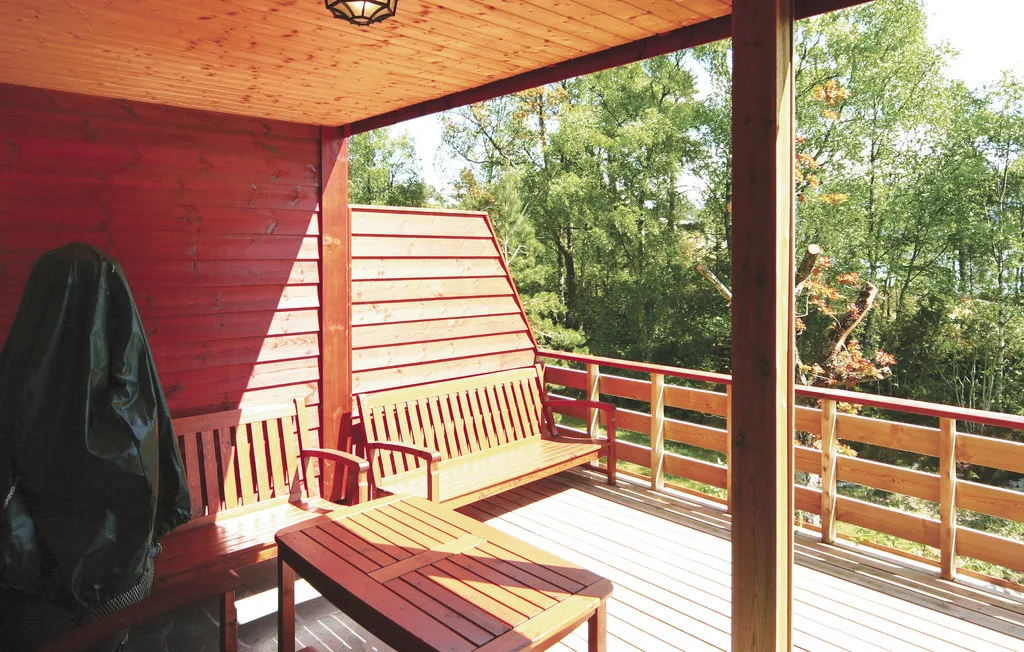 A covered wooden deck with outdoor seating and a leafy view.
