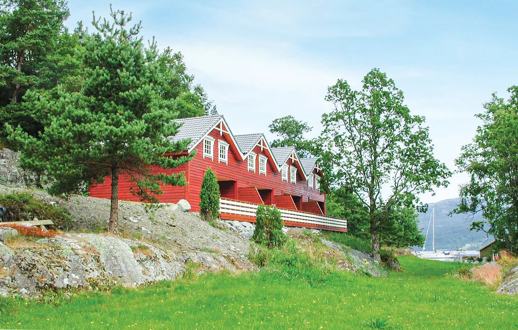 A red wooden building with white trim stands on a grassy hillside among trees.