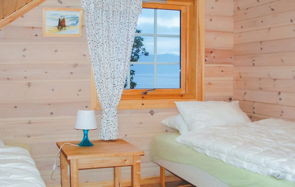A bedroom with a bed beside a wood-framed window and small bedside table.