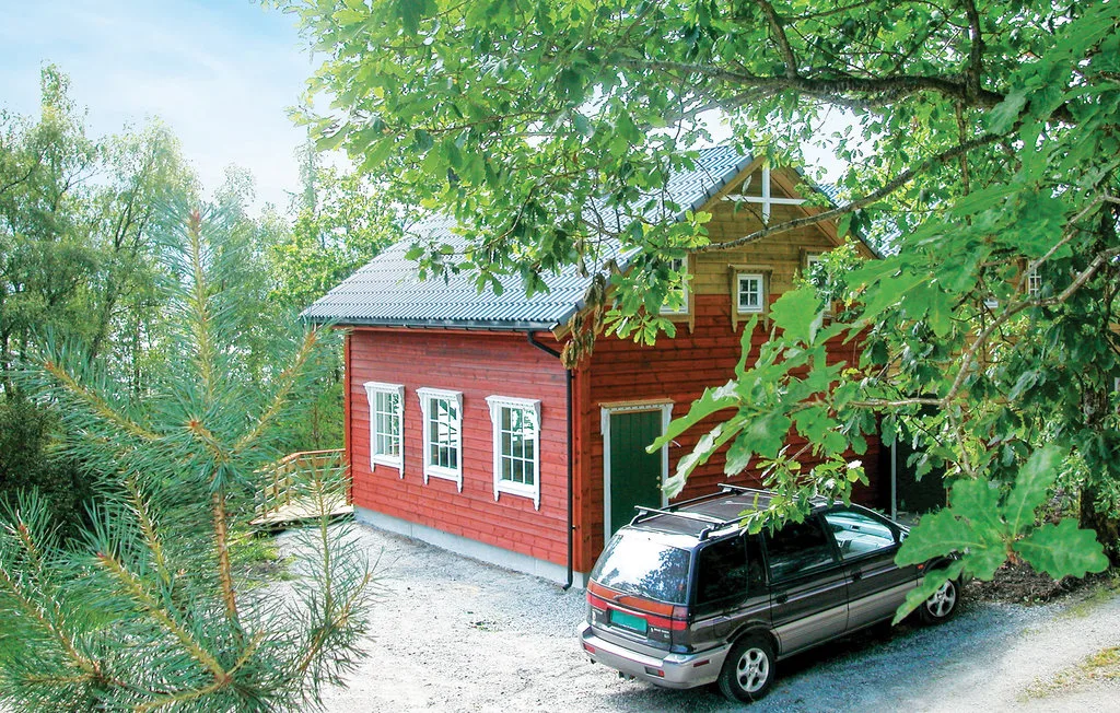 A red wooden cabin stands among trees beside a parked minivan.