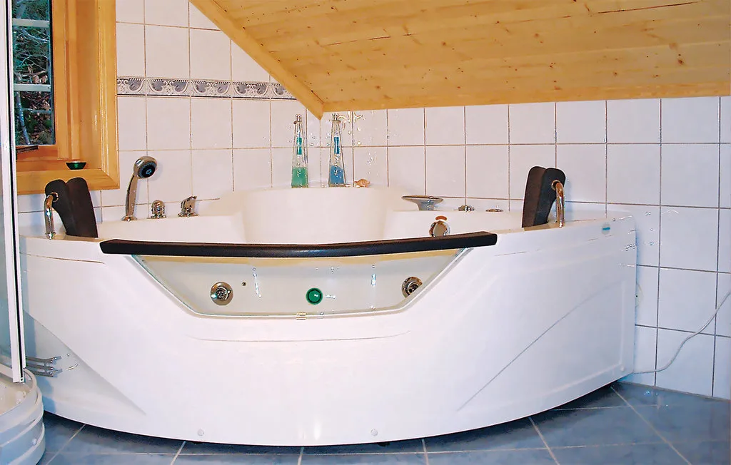 A large bathtub sits beneath a sloped wooden ceiling in a tiled bathroom.