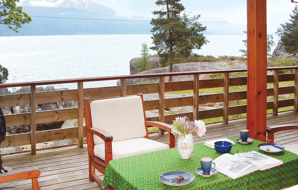 A lakeside deck seating area with a table set beside the wooden railing.
