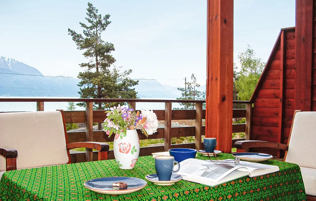 An outdoor dining table on a wooden deck overlooks a lake and distant mountains.