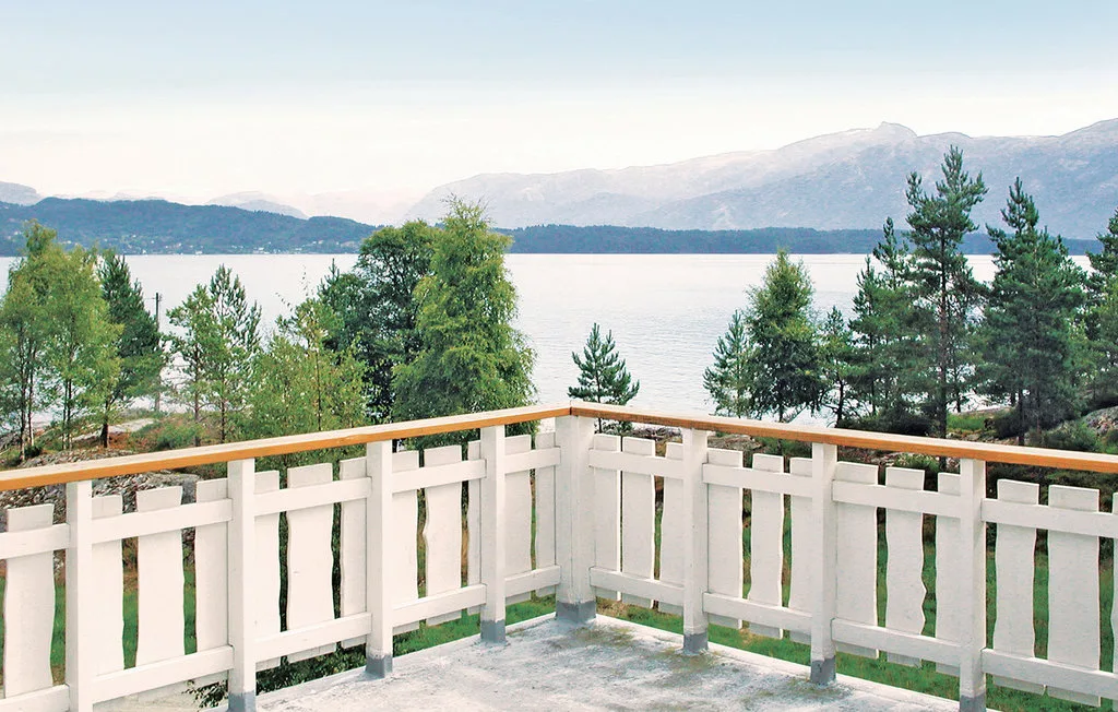 A white-railed deck overlooks a lake, trees, and distant mountains.